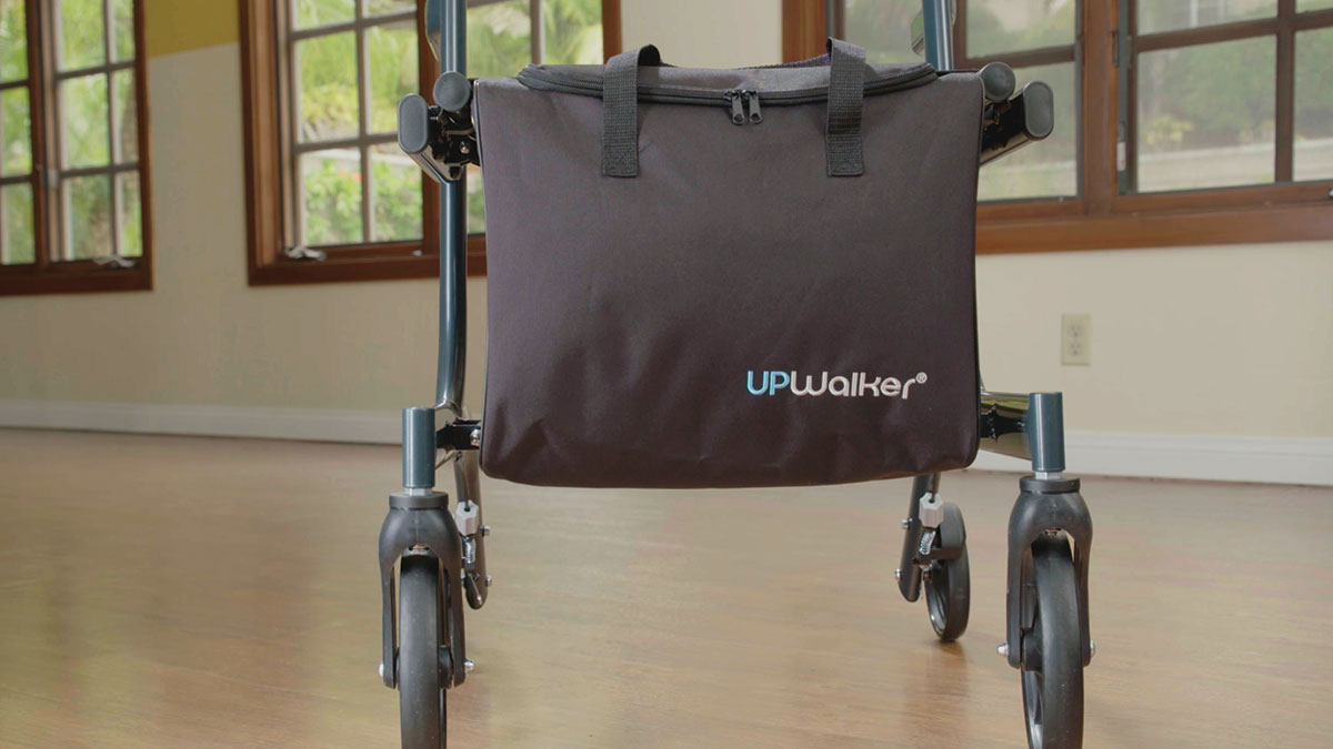 An UPWalker-branded personal walker bag attachment connected low on the frame of an upright walker, hanging below the seat.
